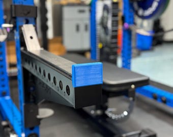 May include: A blue and black weightlifting bench with a blue safety bar and a black weight plate on the floor.