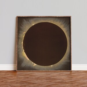 Op de afbeelding: Een ingelijste print van een zonsverduistering, die de corona van de zon laat zien rond een donker, cirkelvormig silhouet van de maan.
