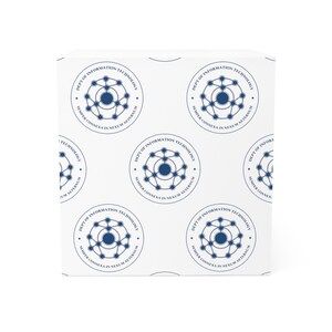 Puede incluir: Una taza de cerámica blanca con asa negra y el texto "But First, Coffee" en negrita negra. La taza se encuentra sobre un fondo borroso, sugiriendo un ambiente acogedor.