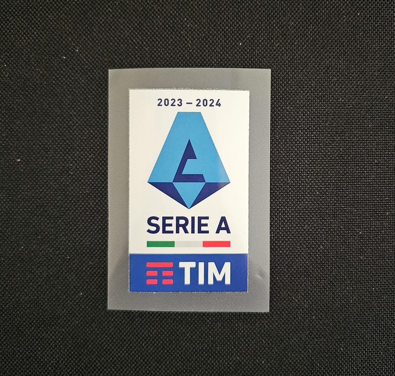 May include: A blue and white patch with the text "2023 - 2024" and "SERIE A" with a logo of a blue triangle with a white letter "A" inside. The patch also has a small Italian flag and the text "TIM" in a white box with three red lines.
