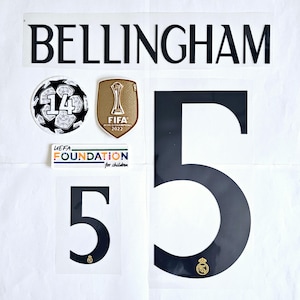 May include: A selection of football-related patches and decals. Features the name "BELLINGHAM" in black, a soccer ball patch with the number 14, a gold FIFA World Champions 2022 patch, and a black number 5. Includes a UEFA Foundation patch.