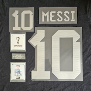 May include: White iron-on patches for a soccer jersey with the number 10, the name "MESSI", and the FIFA World Cup Qatar 2022 logo. There are also patches with the text "POLAND 30 NOVEMBER 2022 STADIUM 974" and "FOOTBALL UNITES the World FIFA".