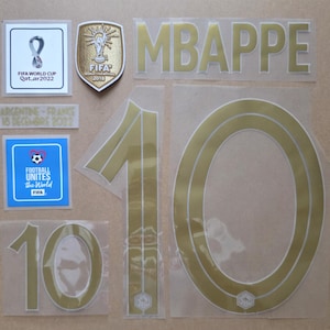May include: A set of gold and white heat transfer decals featuring the name MBAPPE, the number 10 in large and small sizes, a FIFA World Cup Qatar 2022 logo, a 2018 FIFA World Champions shield, a Football Unites the World patch, and a text label.
