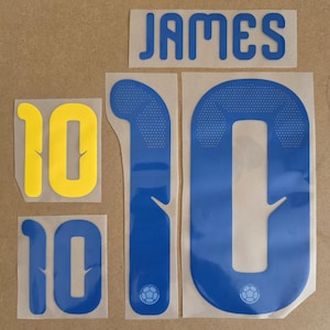 Op de afbeelding: Een set strijkapplicaties met de naam JAMES in het blauw, een groot blauw cijfer 10, een langwerpig blauw cijfer 1, een klein geel cijfer 10 en een klein blauw cijfer 10. Elk ontwerp heeft een gladde afwerking met een klein voetbal-icoon.
