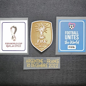 Könnte beinhalten: Drei Patches für ein Fußballtrikot. Der erste Patch ist weiß mit einem goldenen Band und dem Text "FIFA WORLD CUP Qatar2022". Der zweite Patch ist golden mit einer Trophäe und dem Text "FIFA WORLD CHAMPIONS 2018". Der dritte Patch ist blau mit einem Herzen und dem Text "FOOTBALL UNITES the World FIFA".