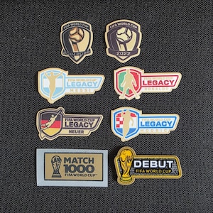 May include: A collection of eight FIFA World Cup themed patches. Two shield-shaped patches feature the trophy and years 2014, 2022. Four rectangular patches display player silhouettes for Messi, Ronaldo, Neuer, and Modric. Includes a Match 1000 and Debut patch.