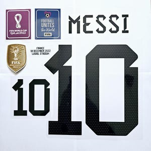 May include: A white football shirt with a black number 10 on the front. The shirt has a black patch with the text "MESSI" on the top. There are also patches with the FIFA World Cup logo and the text "FIFA World Cup Qatar2022" and "Football unites the world FIFA".