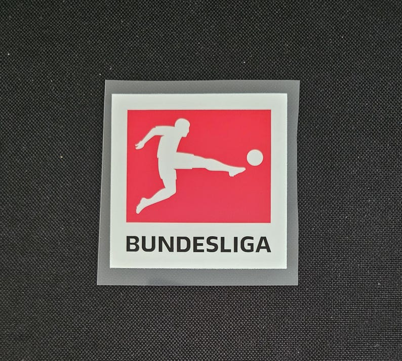 May include: A white silhouette of a soccer player kicking a ball on a red background with the text "BUNDESLIGA" in black below.