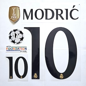 Peut inclure: Un ensemble de patchs thermocollants pour un maillot de football. Les patchs comprennent le nom "MODRIĆ", le numéro "10", un ballon de football avec le numéro "14" et un logo de la Fondation UEFA pour l'enfance.