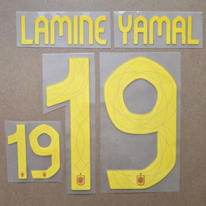 May include: A set of yellow heat transfer decals featuring the name LAMINE YAMAL and the number 19 in two sizes. The designs include thin, curved line patterns and a small red and gold Spanish national football team crest at the base.