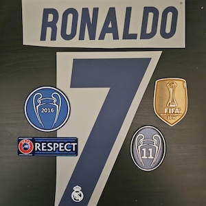 May include: A white and blue soccer jersey with the name "RONALDO" and the number "7" printed on the front. The jersey has several patches, including a gold FIFA World Champion 2016 patch, a blue UEFA Champions League 2016 patch, a blue UEFA Champions League 11 patch, and a red and blue patch that says "RESPECT".