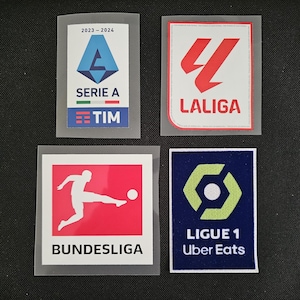 May include: Four different soccer league patches. The top left patch is blue, white, and red with the text "Serie A 2023-2024 TIM". The top right patch is white with a red logo and the text "LaLiga". The bottom left patch is white with a red background and the text "Bundesliga". The bottom right patch is blue with a green logo and the text "Ligue 1 Uber Eats".