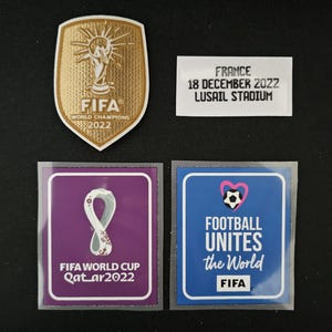 Op de afbeelding: Vier patches voor een voetbaltenue. De linker bovenste patch is goud met een trofee en de tekst "FIFA World Champions 2022". De rechter bovenste patch is wit met de tekst "Frankrijk 18 december 2022 Lusail Stadium". De linker onderste patch is paars met een wit lint en de tekst "FIFA World Cup Qatar2022". De rechter onderste patch is blauw met een roze hart met een voetbal en de tekst "Football Unites the World FIFA".