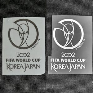 May include: Two rectangular stickers featuring the 2002 FIFA World Cup logo. The logo includes a stylized design within a circle, the text "2002 FIFA WORLD CUP KOREA JAPAN", and the FIFA copyright.