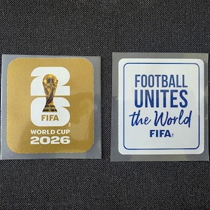 May include: Two square stickers. The left sticker is gold with the white text 26, the FIFA World Cup trophy, and the text FIFA World Cup 2026. The right sticker is white with a blue border and the blue text FOOTBALL UNITES the World and FIFA.