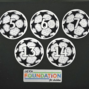 May include: Five black and white soccer ball stickers with numbers 5, 6, 7, 13, and 14 printed on them. The stickers have a UEFA Foundation for children logo.