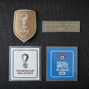 May include: A collection of four soccer-themed patches including a gold FIFA 2018 World Champions shield, a rectangular patch reading ARGENTINE - FRANCE 18 DECEMBRE 2022, a FIFA World Cup Qatar 2022 logo patch, and a blue Football Unites the World patch.