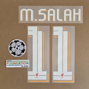 May include: A set of iron-on heat transfer decals featuring the name M. SALAH in white with orange outlines, two large number 11 digits with the Liverpool FC crest, a circular patch with the number 6, and a rectangular UEFA Foundation for children patch.