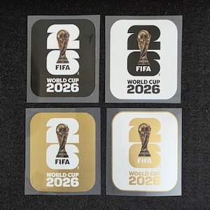 Puede incluir: Cuatro pegatinas cuadradas con el logotipo de la Copa Mundial de la FIFA 2026. El diseño incluye el número 26 con el trofeo reemplazando al cero, y el texto FIFA WORLD CUP 2026. Las pegatinas son negras, blancas, doradas y blancas con texto dorado.