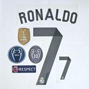 May include: A collection of sports-themed decals and patches. Includes the name "RONALDO" in black block letters, the number "7" in gray, and various team and championship badges. The FIFA World Champions 2014 patch is also visible.