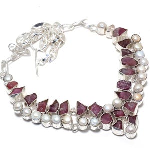 Puede incluir: Un collar de plata con un diseño en forma de V adornado con piedras preciosas rosas y blancas. El collar tiene un cierre de langosta.