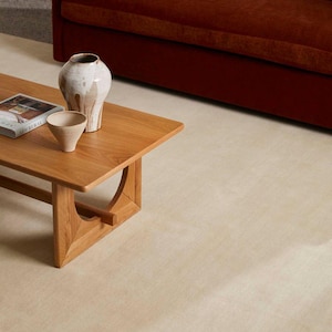Puede incluir: Una mesa de centro de madera de color marr&oacute;n claro con una superficie rectangular y soportes arqueados, que presenta un jarr&oacute;n de cer&aacute;mica alto en blanco y marr&oacute;n, un cuenco beige texturizado y un libro titulado New Rural.