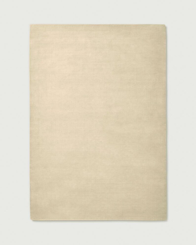 Puede incluir: Una alfombra rectangular de color beige claro s&oacute;lido. La alfombra presenta una textura tejida plana y uniforme en toda su superficie, con bordes rectos y limpios, y un tono neutro y consistente que cubre toda la forma rectangular.