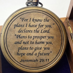 May include: A round, antique-style brass pocket watch pendant featuring a dark, textured finish. The front cover is engraved with the text: For I know the plans I have for you, declares the Lord. Plans to prosper you and not to harm you, plans to give you hope and a future, Jeremiah 29:11.