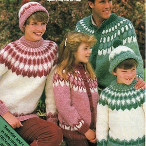 Puede incluir: Una familia lleva jerséis y gorros de punto a juego con un patrón escandinavo tradicional. Los jerséis son blancos con detalles rojos y verdes, y los gorros son blancos con un pompón en la parte superior. Los jerséis están disponibles en tallas de 24 a 46 pulgadas (60-115 cm).