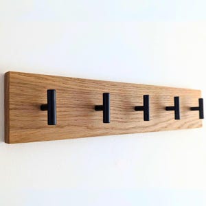 May include: A wooden wall-mounted coat rack with five black T-shaped hooks.