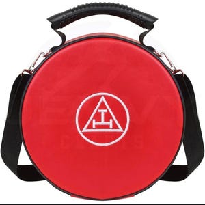 Könnte beinhalten: Eine runde, rote Tasche mit schwarzem Griff und Schultergurt. Die Tasche hat ein weißes Emblem in einem Kreis auf der Vorderseite. Das Emblem ist ein Dreieck mit einer horizontalen und einer vertikalen Linie in der Mitte.