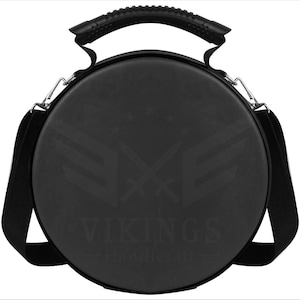 May include: A black, round carrying case with a handle and shoulder strap. The case features a logo with crossed swords and the text "VIKINGS Handicraft". The handle is textured for grip, and the strap is adjustable.