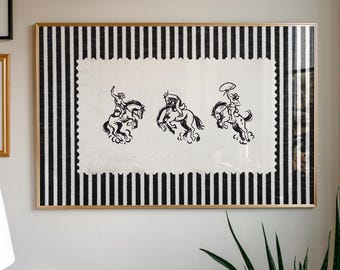 May include: Framed artwork featuring three black and white illustrations of cowboys riding bucking horses. The artwork is set against a black and white striped background and framed in gold. The artwork is mounted on a white background.