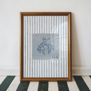 Add a bold statement to your space with this vintage striped rodeo print. Featuring retro blue and white stripes with a rustic western vibe, this cowboy poster is perfect for adding western bedroom wall art flair. The charming retro horse print blends seamlessly into rustic mid century modern home decor styles and makes a cute accent for dorm decor. Ideal for rodeo lovers, cowboy fans, and anyone who loves unique vintage western style.