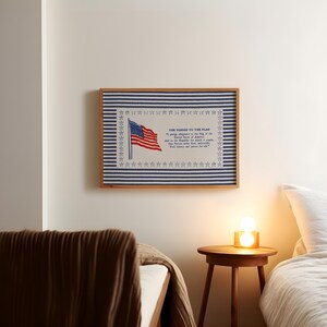 May include: A rectangular framed wall art piece featuring a blue and white horizontal striped background. The center displays an American flag illustration and the text of The Pledge to the Flag, surrounded by a border of small blue stars.