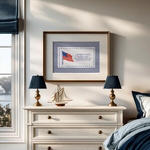May include: A framed print featuring the Pledge of Allegiance and an American flag illustration, centered above a white dresser. The artwork is bordered by a blue and white striped pattern and a row of stars, displayed in a gold-toned frame.