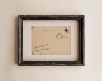 May include: Framed vintage postcard with the text "POSTCARD" and a stamp featuring an American flag. The postcard has the handwritten phrase "Land of the free because of the brave." The frame is dark brown.