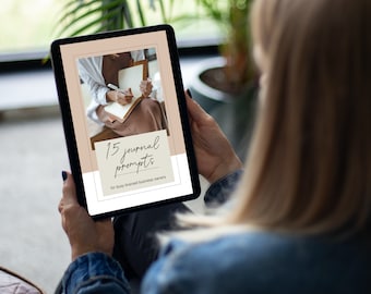 Könnte beinhalten: Ein digitales Tablet zeigt einen hellbraunen Hintergrund mit dem Text "15 journal prompts for busy-brained business owners". Eine Frau hält das Tablet in ihren Händen.