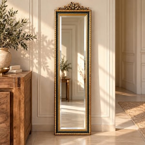 Könnte beinhalten: Ein hoher, rechteckiger Standspiegel mit einem schwarz-goldenen Rahmen, einer seilartigen Innenkante und einem verzierten, geschnitzten goldenen Ornament an der Oberseite. Der Spiegel hat eine facettierte Glasfläche und steht vertikal an der Wand.