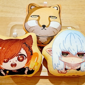 May include: Three plush keychains featuring cartoon characters. The first keychain is a fox with orange fur and a white muzzle. The second keychain is a girl with brown hair and a black outfit. The third keychain is a girl with blue hair and a white dress.