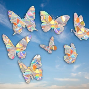 May include: Seven iridescent butterfly stickers with a stained glass design. The butterflies are various shades of blue, green, purple, and orange. The stickers are on a blue sky background with white clouds.