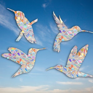 May include: Four iridescent hummingbird silhouettes against a blue sky with white clouds. The hummingbirds are made of stained glass with a rainbow of colors.