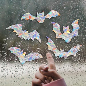 May include: A set of six iridescent holographic bat stickers. The bats are various sizes and are arranged on a window with raindrops.