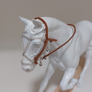 May include: White horse figurine wearing a brown leather halter with silver chain and bells.