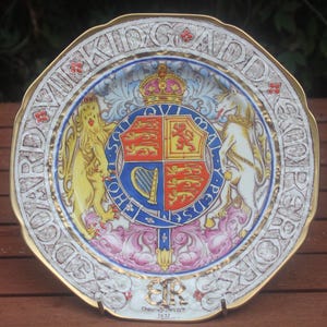 May include: A decorative ceramic plate featuring the British Royal Coat of Arms with a lion and unicorn, a central crown, and the text "Honi Soit Qui Mal Y Pense" on a blue garter. The rim displays the text "VIKING ADD SKOOPER WORKS" and "ER 1952".