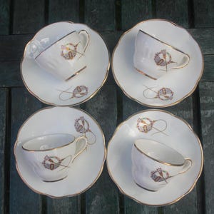 May include: Four white teacups and saucers with gold trim. Each cup and saucer has a floral design with gold accents.