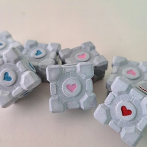 May include: Six grey cube-shaped objects with a heart design on each side. The hearts are in different colours, including pink, blue, and red.