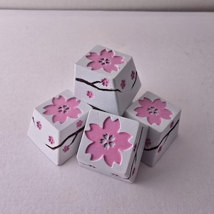 Può includere: Quattro tasti bianchi con disegni di fiori di ciliegio rosa. I tasti hanno un design in rilievo con un ramo e fiori più piccoli.