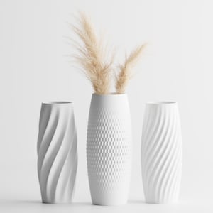 May include: Three white vases with distinct textures. The two outer vases feature a diagonal spiral pattern, while the central vase has a geometric grid texture. The central vase contains two beige, feathery, dried botanical stems.