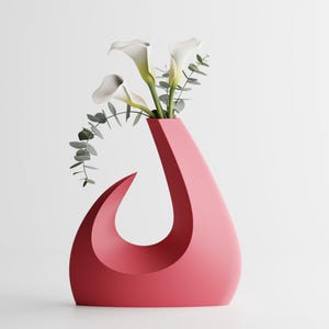 May include: A contemporary, coral-coloured vase with a distinctive, curved design. The vase contains white calla lilies and green eucalyptus branches. The vase has a smooth, matte finish and is set against a white background. A decorative floral arrangement.